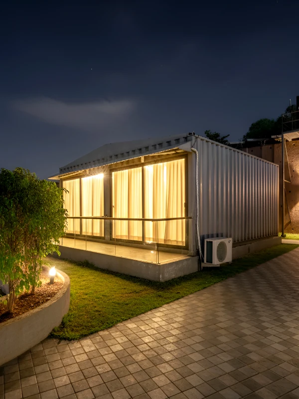 Container Cabin Stay – Unique Room at Orchid Panchgani Container cabin room with glass walls glowing at night on landscaped lawn at Orchid Hotel Panchgani