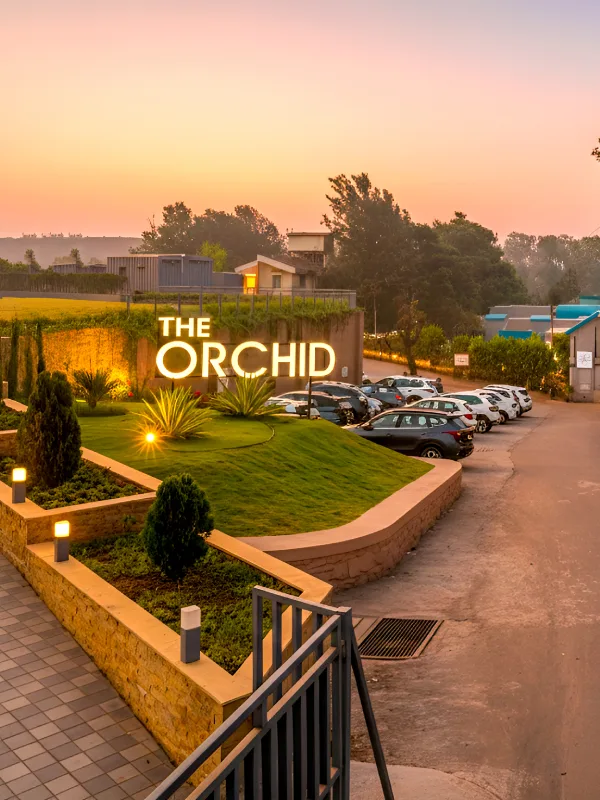 Orchid Hotel Panchgani Entrance – Book Best Hotel Near Table Land The Orchid Hotel Panchgani entrance with illuminated signage, landscaped garden, and parking at sunset