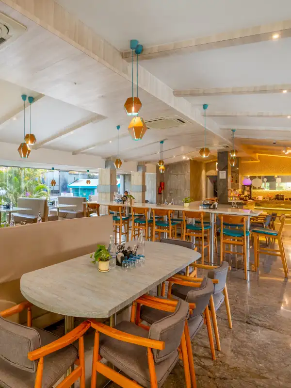 Restaurant Dining – Multi-Cuisine Meals at Orchid Panchgani Restaurant dining area with wooden tables, pendant lights, and poolside view at Orchid Hotel Panchgani