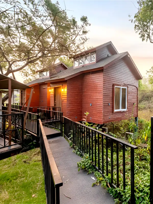 Wooden Cottage Suite – Book Nature Stay at Orchid Panchgani Wooden cottage suite exterior with walkway and lush greenery at sunset, Orchid Hotel Panchgani near Table Land