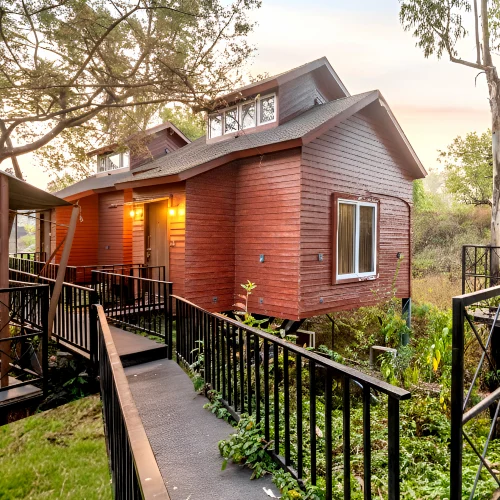 Wooden Cottage Suite – Book Nature Stay Orchid Panchgani Wooden cottage suite with elevated walkway and greenery at sunset, Orchid Hotel Panchgani