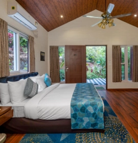 Wooden Cottage Suite King Bedroom with Garden View - Orchid Hotel Panchgani King-size bedroom with teal accents, ceiling fan and lush garden view in Wooden Cottage Suite at Orchid Hotel Panchgani