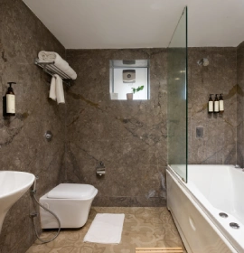 Strawberry Club Room Luxury Bathroom with Bathtub - Orchid Hotel Panchgani Strawberry Club Room luxury bathroom with marble walls, bathtub, glass shower partition and wall-hung toilet at Orchid Hotel Panchgani