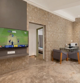 Strawberry Club Room Smart TV and Kitchenette - Orchid Hotel Panchgani Strawberry Club Room interior with wall-mounted smart TV, textured stone wall and kitchenette counter at Orchid Hotel Panchgani